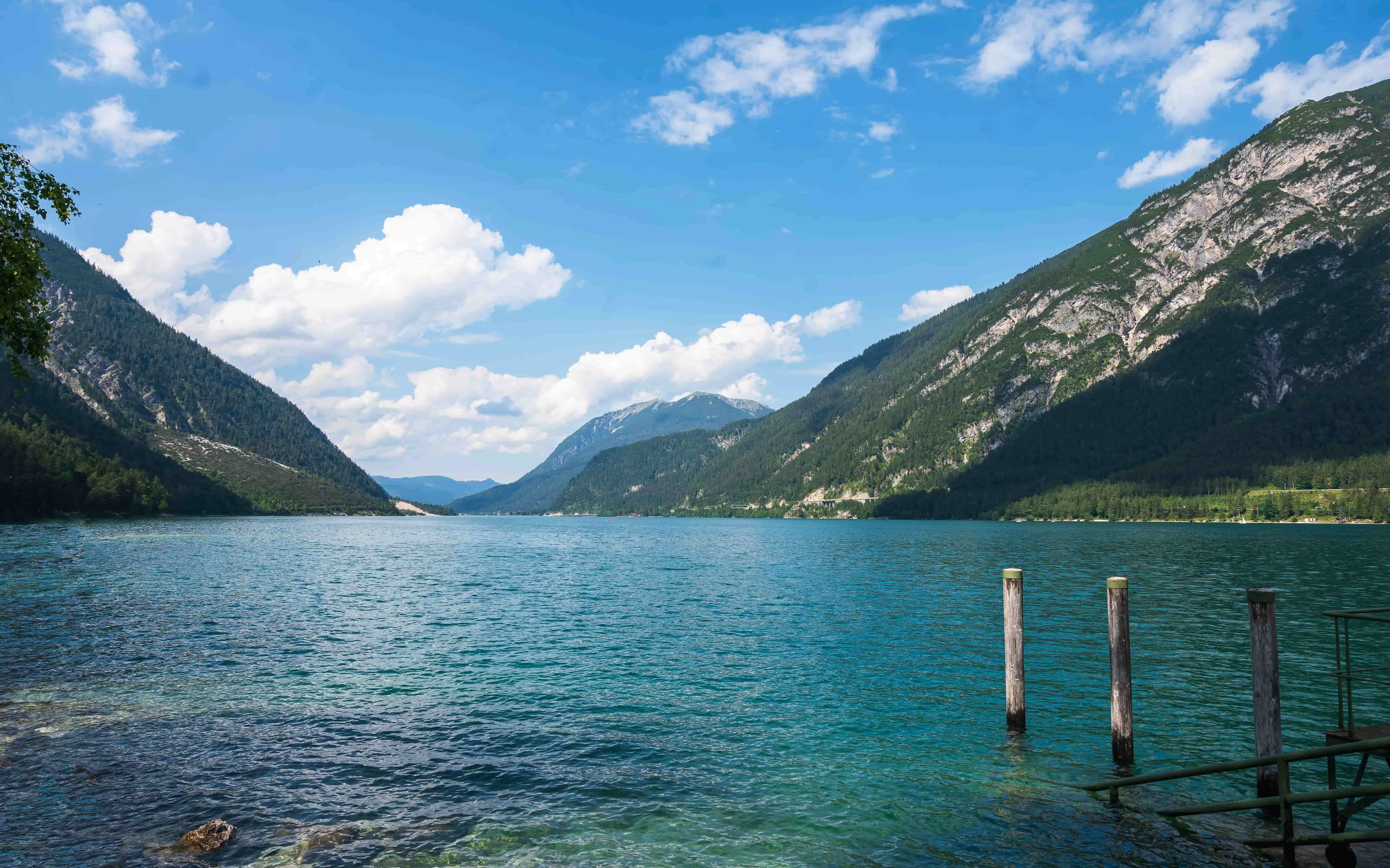 View of a large lake, with mountains either side and in the distance. A cloudy but blue sky.