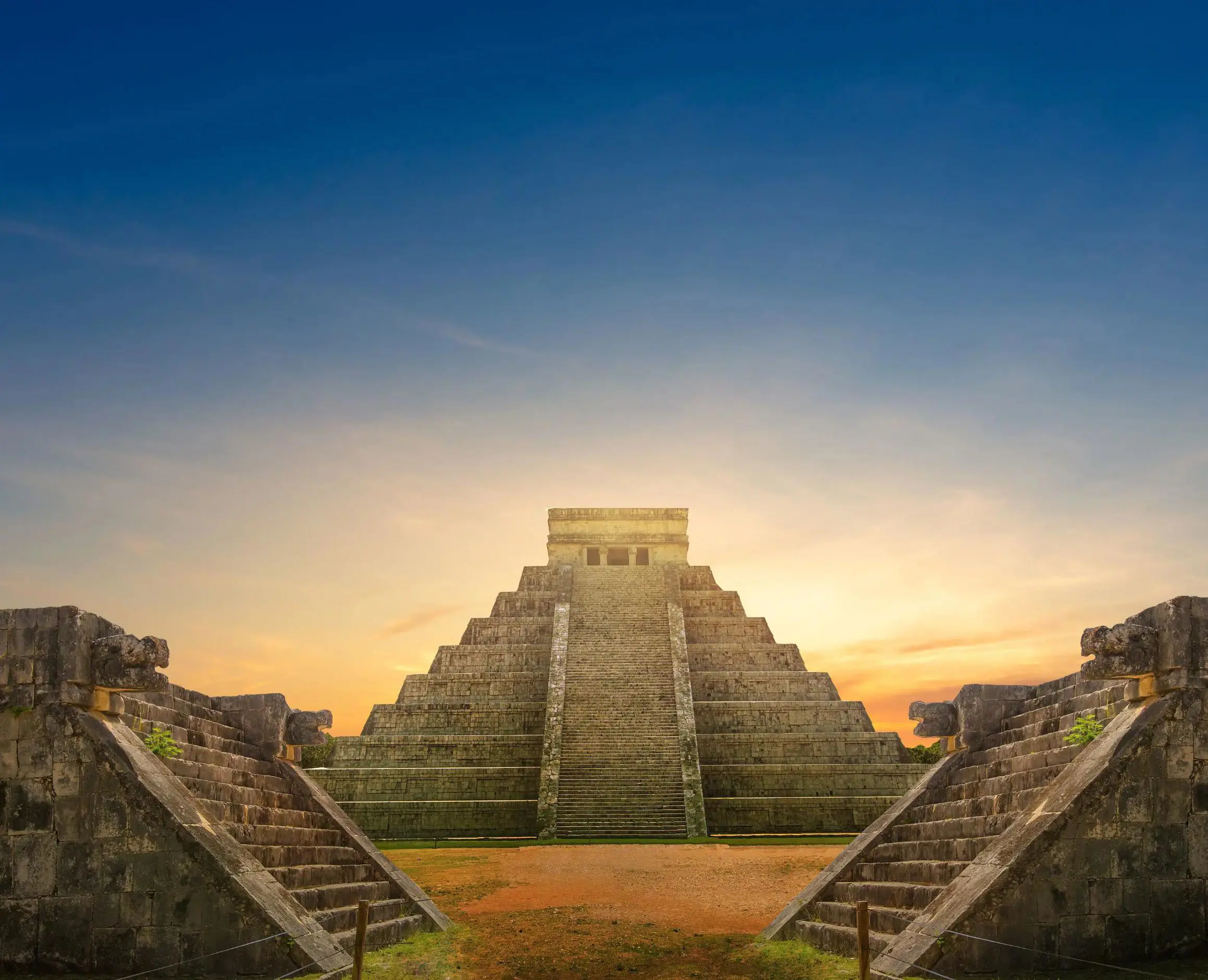 The ancient Mayan pyramid of Chichen Itza at sunset, with stairs leading up the centre and a clear sky fading from orange to deep blue