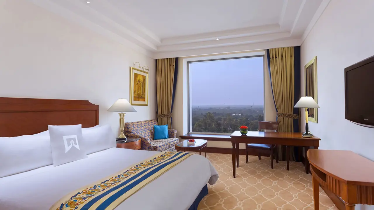 Elegant guest room at Sheraton New Delhi, featuring a king-sized bed, classic furnishings, large window with a city view, and warm, neutral décor