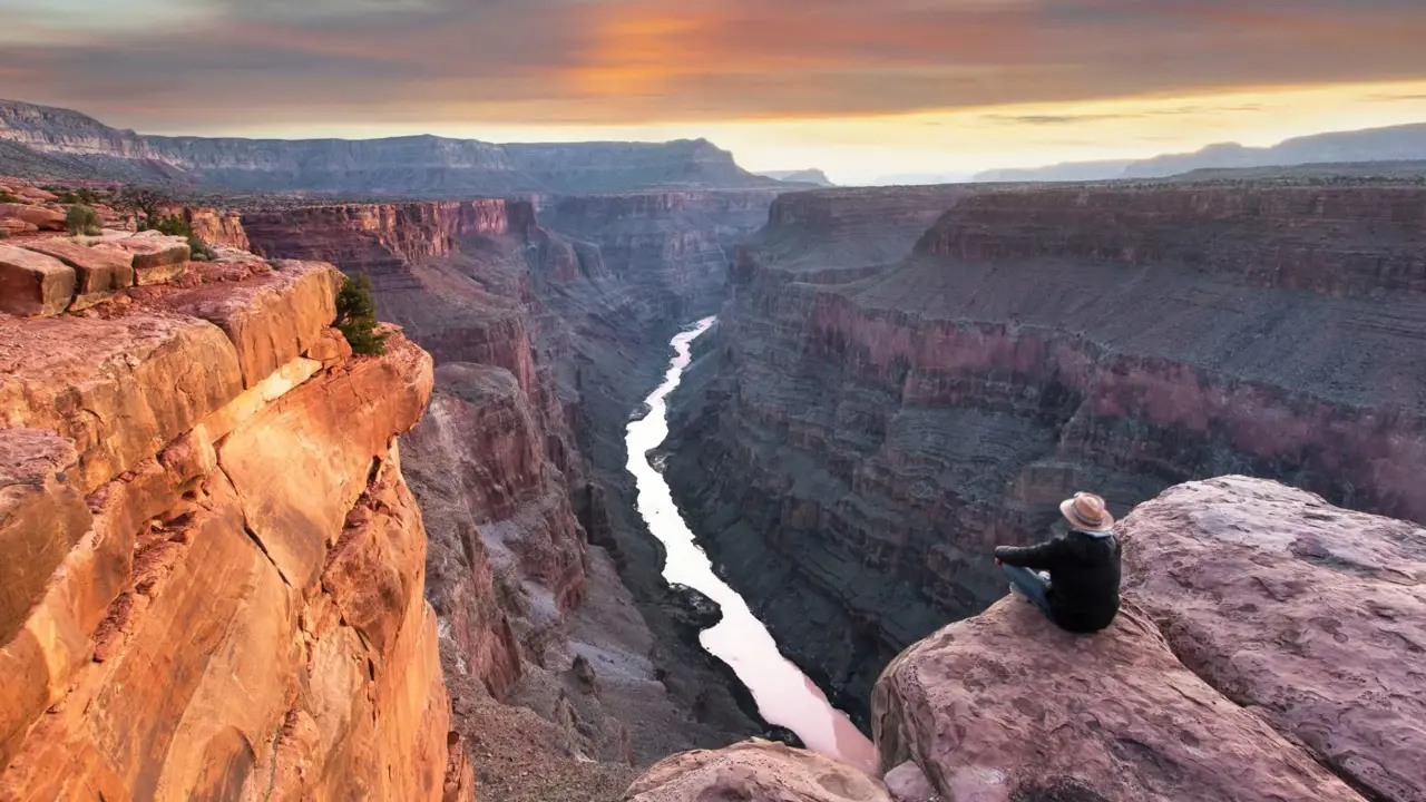 Toroweap Point at the Grand Canyon, with a person sitting near the edge, overlooking the vast canyon landscape as the sun sets