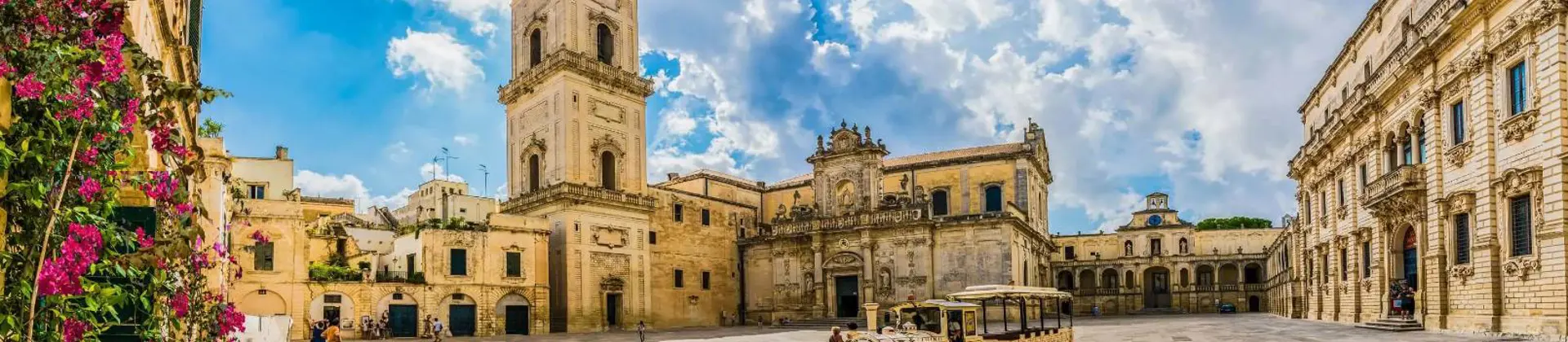 A square in Lecce, Italy, featuring a historic tower and a land train for tourists