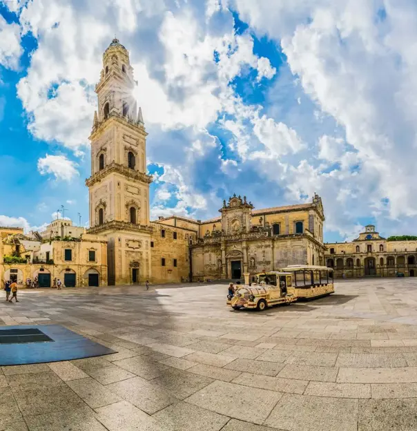 A square in Lecce, Italy, featuring a historic tower and a land train for tourists