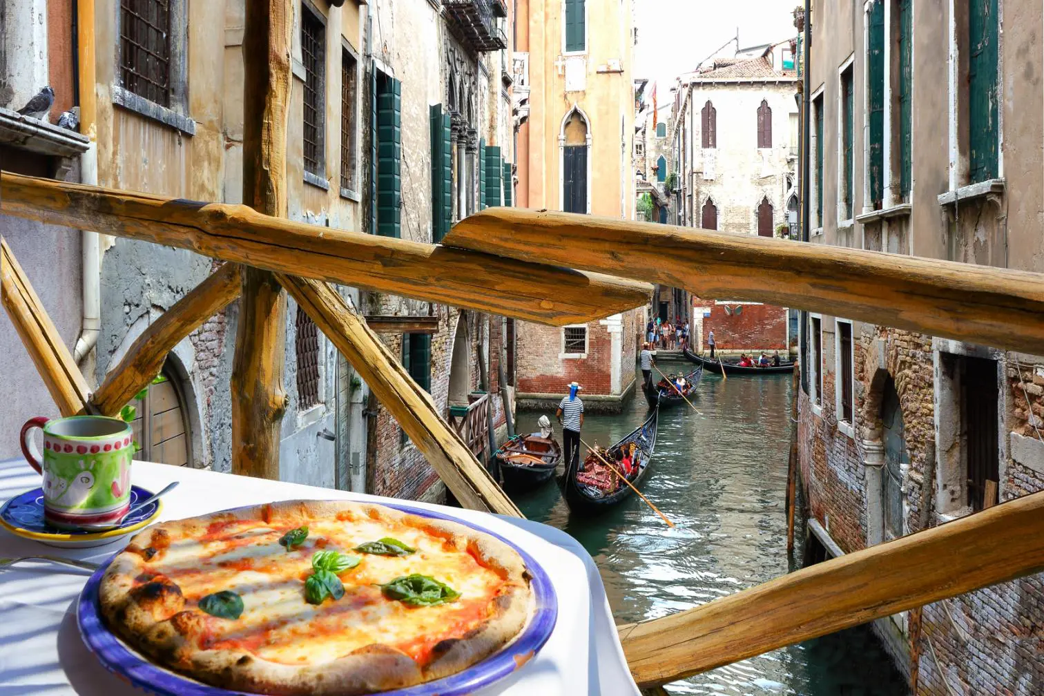 Gondolas gliding along a narrow canal beside a pizza restaurant in Venice, Italy