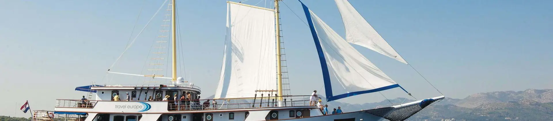 Shot of a sailing boat on water. With mountains to the right in the distance.