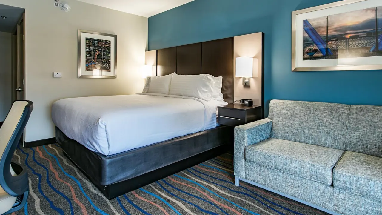 Modern guest room at Holiday Inn and Suites Downtown Chattanooga, featuring a king bed, sleek furnishings, vibrant carpet, and a cosy sofa for added comfort
