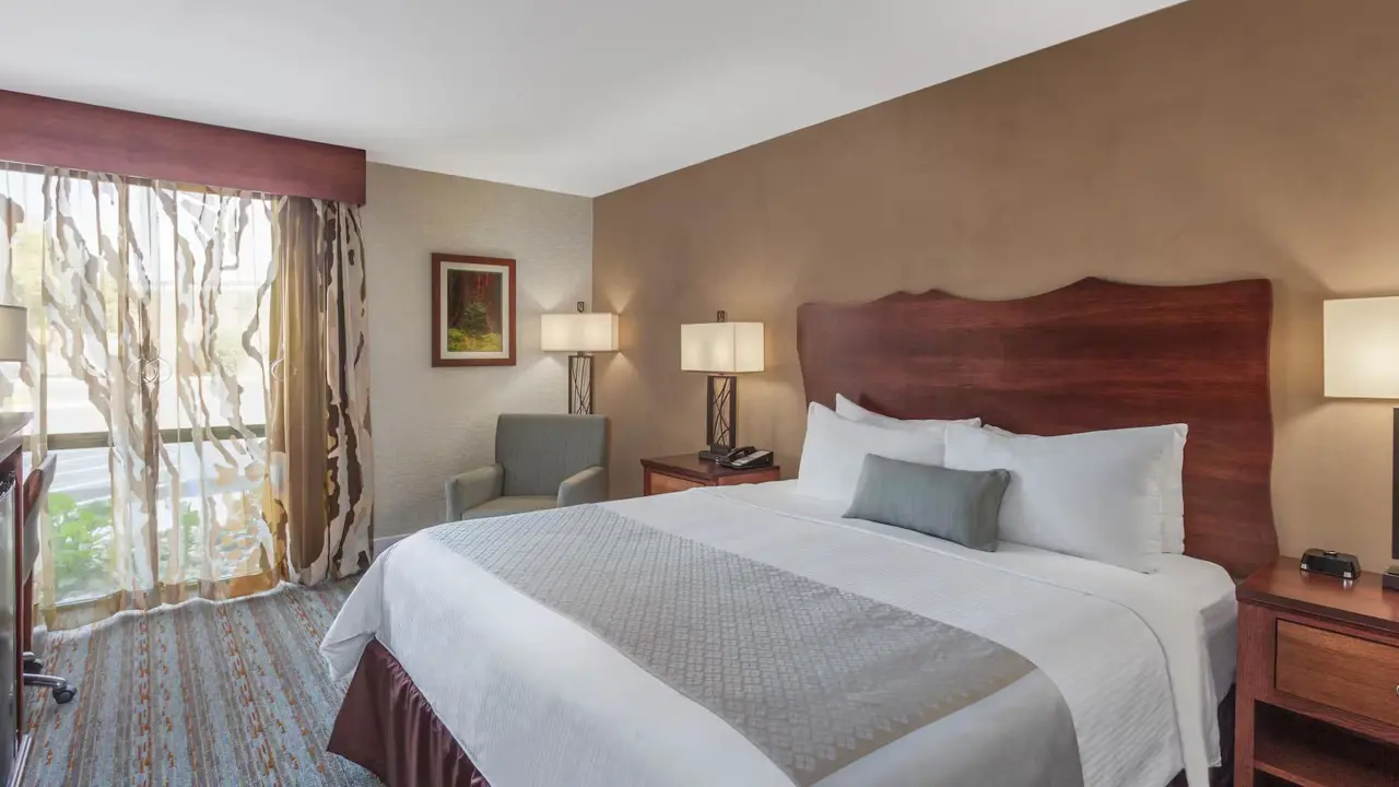 Spacious king bedroom at the Wyndham Hotel, Visalia, featuring a large bed with white linens, contemporary furnishings, and soft, warm lighting