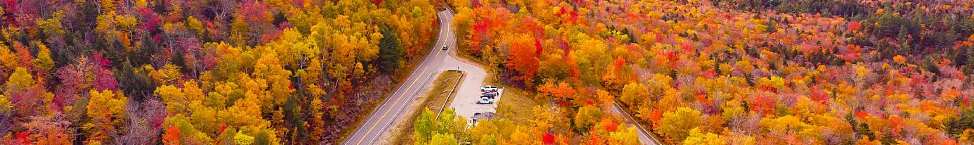 Kancamagus Highway in New Hampshire lined with vibrant autumn foliage, featuring a winding road surrounded by trees in shades of red, orange, and yellow