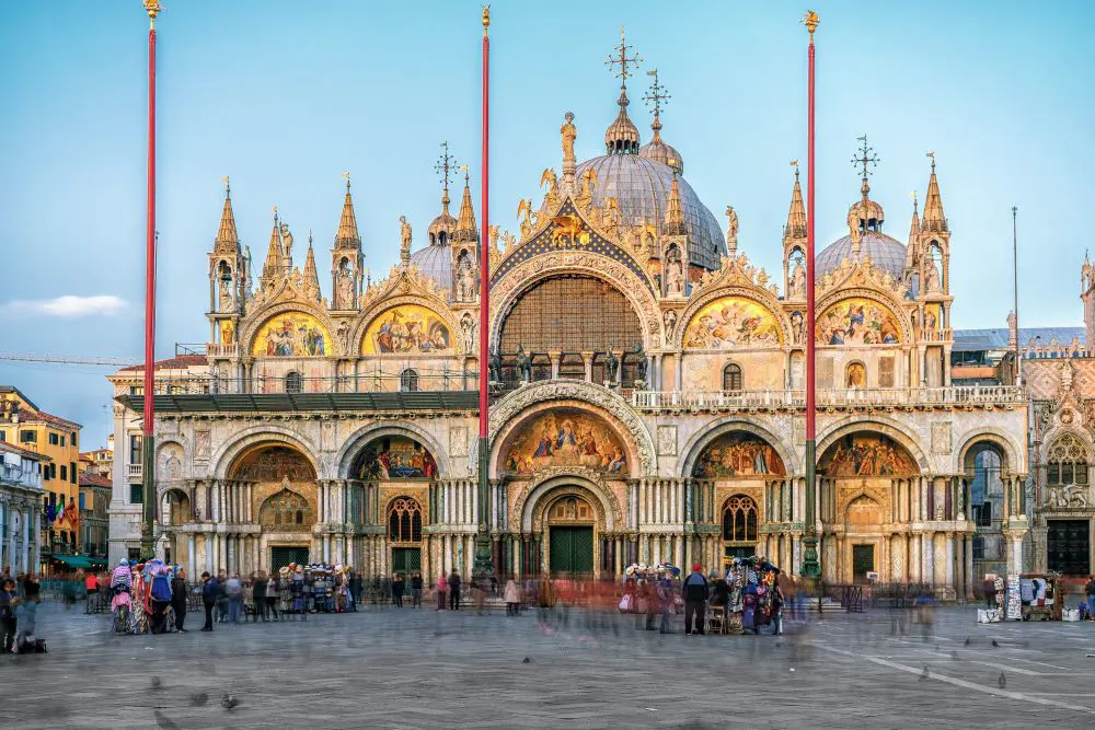 Exterior view of Saint Mark’s Basilica in Venice, Italy, showcasing its ornate façade with domes, arched windows, and detailed mosaics, reflecting Byzantine architectural style