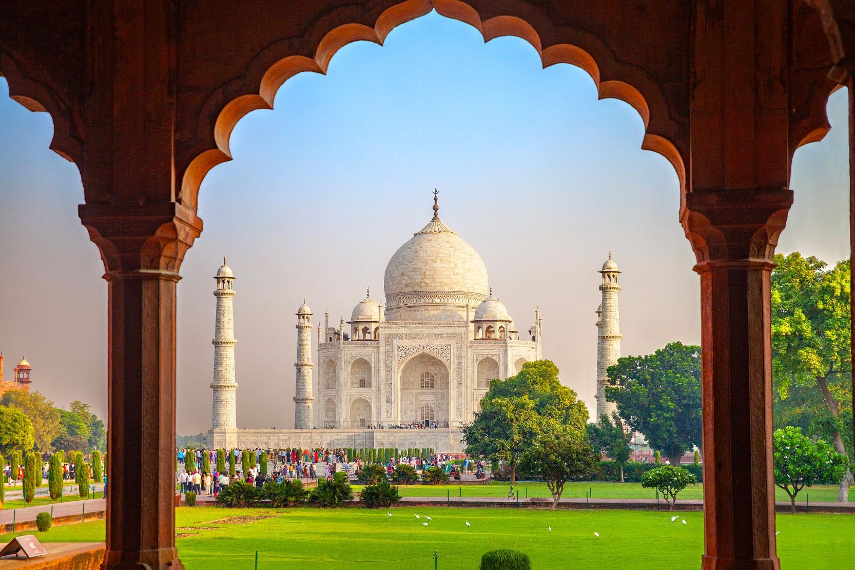 The Taj Mahal framed by an ornate archway, with green gardens in the foreground