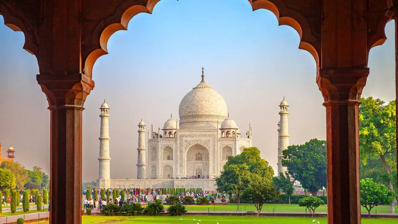 The Taj Mahal framed by an ornate archway, with green gardens in the foreground