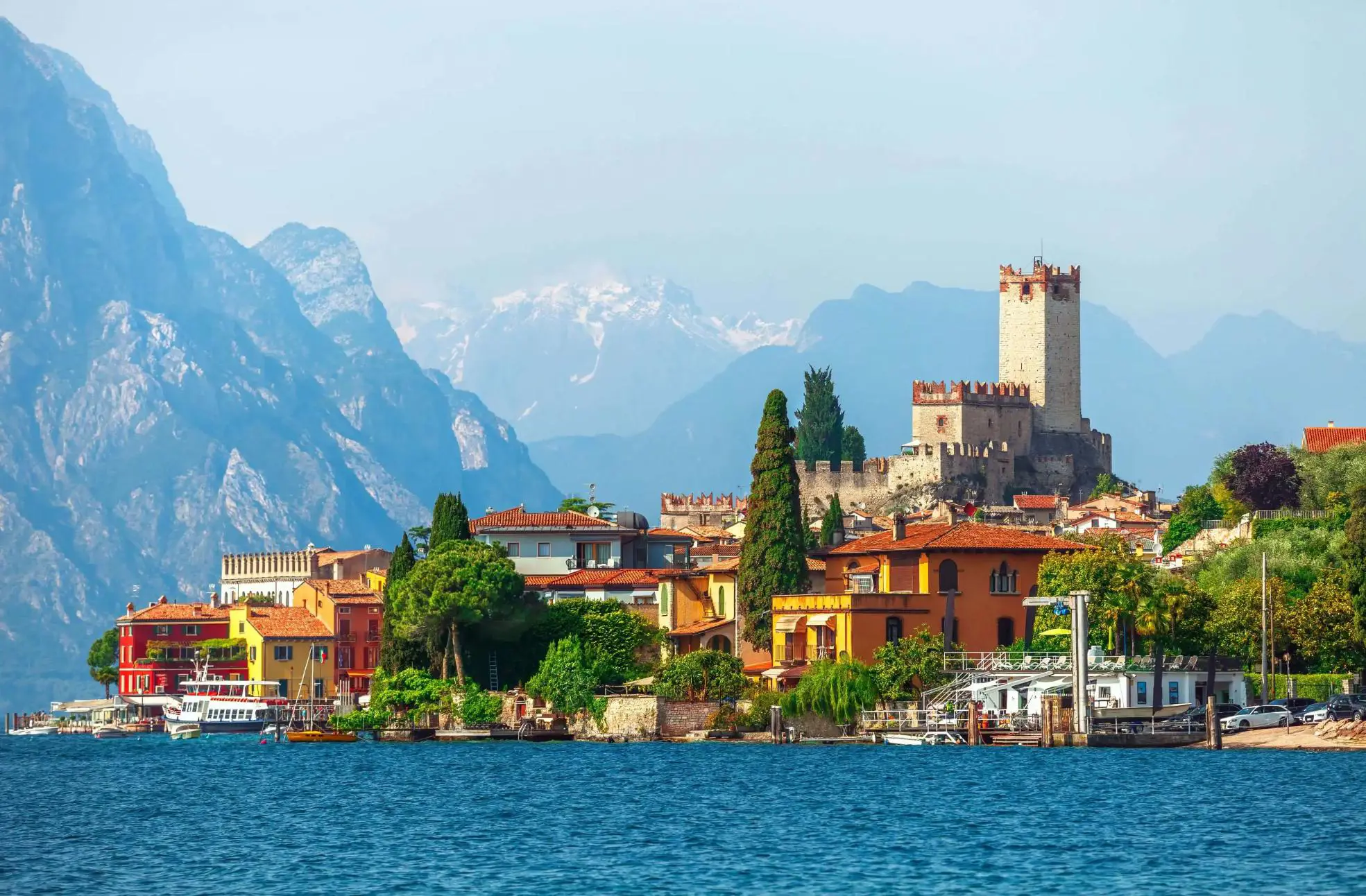 A scenic view of Malcesine on the shores of Lake Garda, Italy, with historic buildings, a medieval castle, and mountains in the background