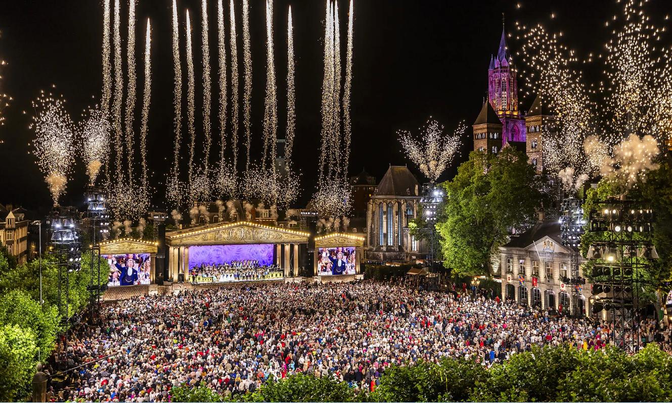 André Rieu performing in Maastricht’s Vrijthof Square, with his orchestra on stage and colourful fireworks lighting up the night sky
