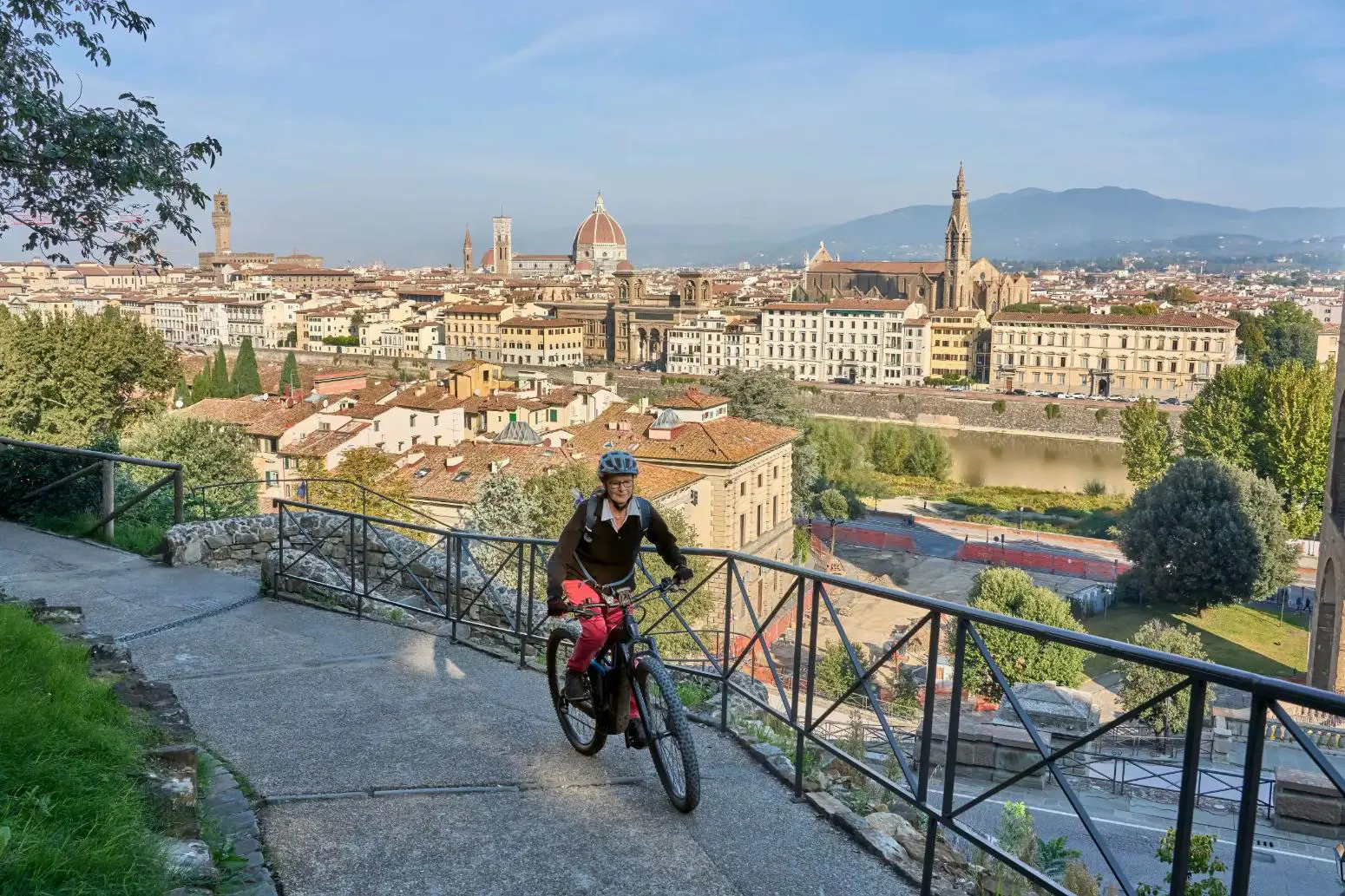 A woman cycling along a pathway on a mountain in Florence, with a view of the city in the background