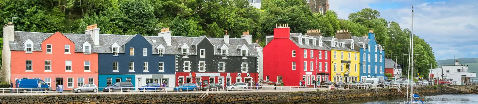 Colourful buildings along the waterfront in Tobermory, Isle of Mull, with a sailboat on the water 
