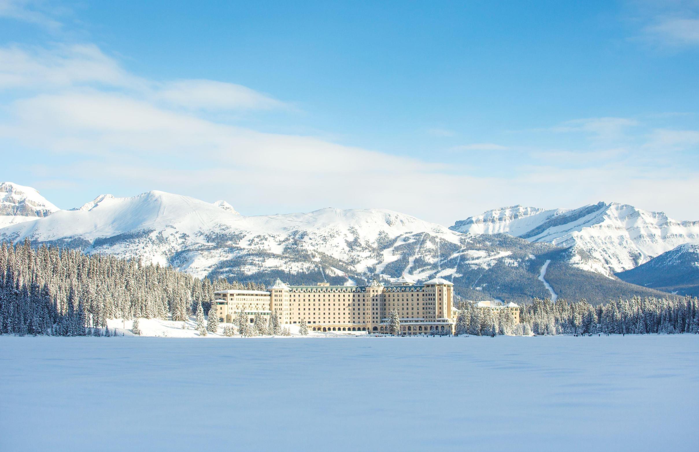 Fairmont Chateau, Lake Louise surrounded by snow-covered trees and mountains under a clear blue sky in winter