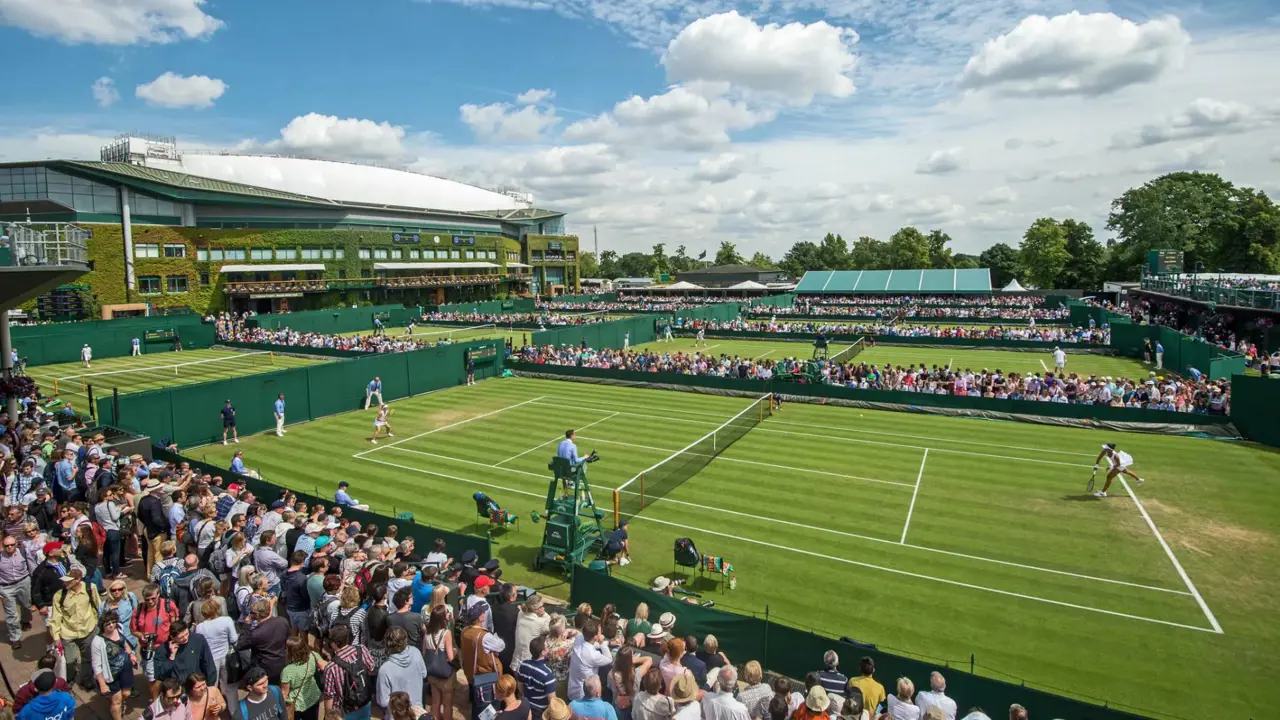 Crowds watching tennis matches on the grass courts at Wimbledon under a blue sky