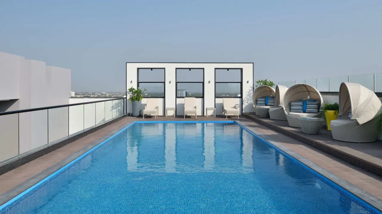 Rooftop swimming pool at Novotel Jodhpur with lounge chairs and cabana seating under a clear blue sky