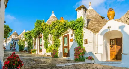 View of traditional white Trulli houses with conical stone roofs in Alberobello, Apulia, Italy, under a clear blue sky