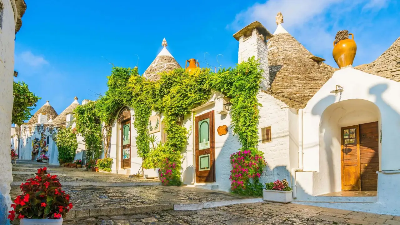 View of traditional white Trulli houses with conical stone roofs in Alberobello, Apulia, Italy, under a clear blue sky