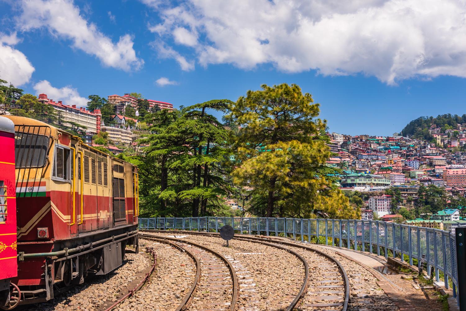 The heritage toy train arrives in Shimla, India, passing by vibrant, colourful buildings in the background