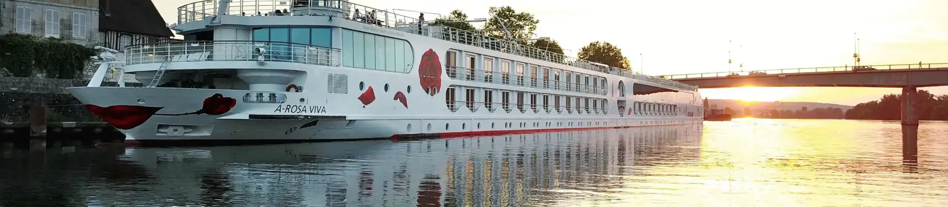 A-ROSA VIVA cruise ship on a calm city river at sunset, with a bridge in the background
