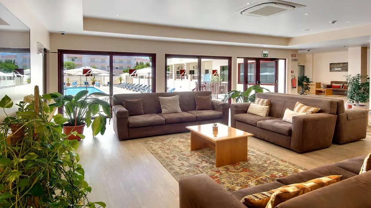 Bright, modern hotel lobby at Hotel Alba in Monte Gordo, Portugal, featuring comfortable lounge seating and large windows overlooking the pool area