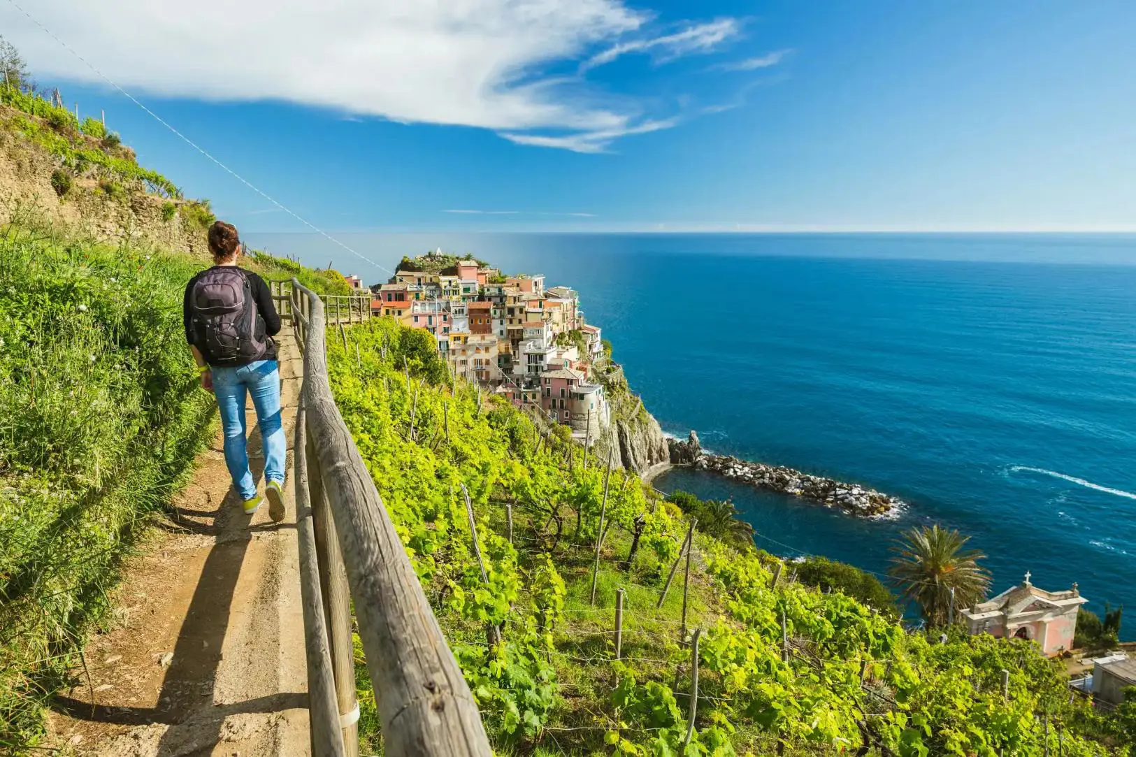 A person walking along a cliffside path in Cinque Terre, overlooking colourful buildings and the blue sea