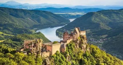 Ruins of a medieval castle perched on a rocky hilltop overlooking the Danube River in the Wachau Valley, Austria, surrounded by lush green hills and distant mountains