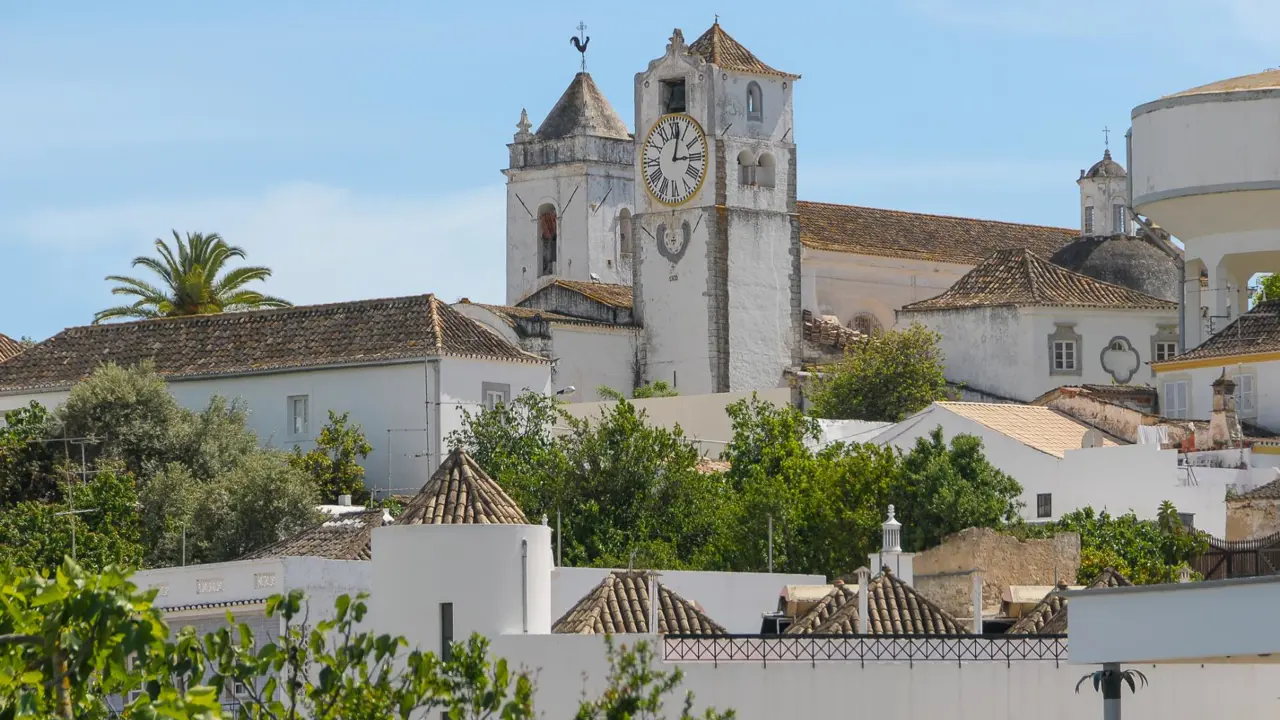 Traditional whitewashed clock tower surrounded by trees and town buildings with tiled roofs in Tavira on the Algarve