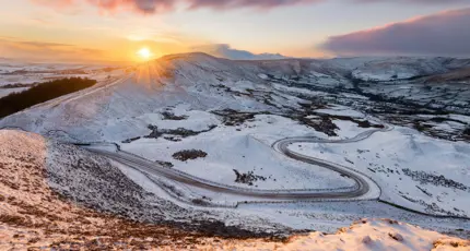 View of the Peak District at winter, with snowy mountains and the sun creeping over the edge of the land