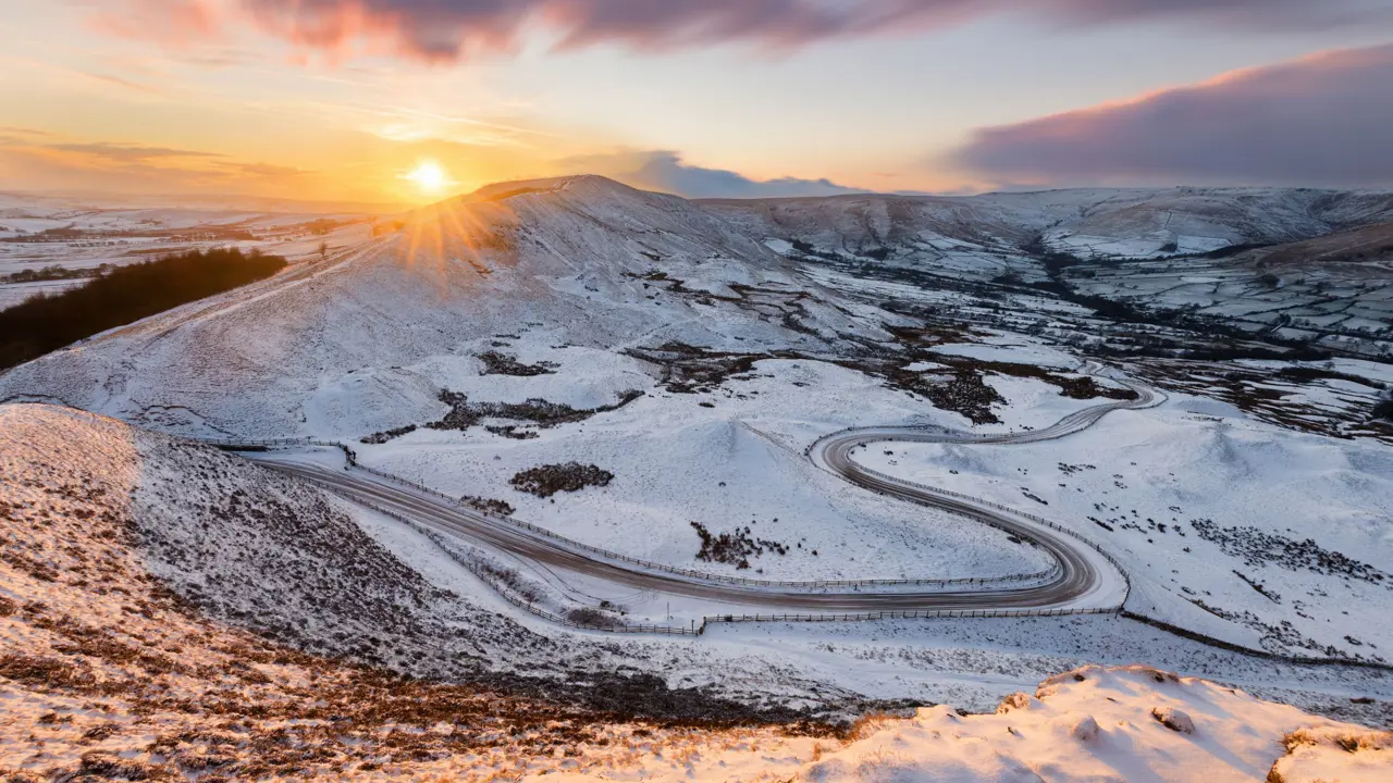 View of the Peak District at winter, with snowy mountains and the sun creeping over the edge of the land