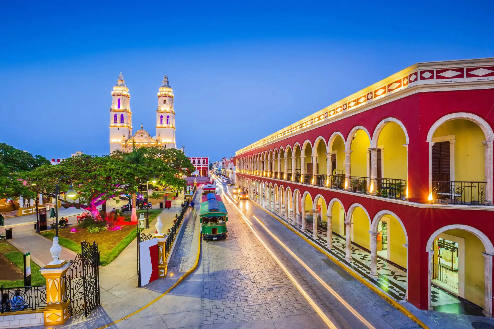 Brightly lit colonial buildings and a cathedral illuminate the street of the historic town of Campeche in Mexico during twilight