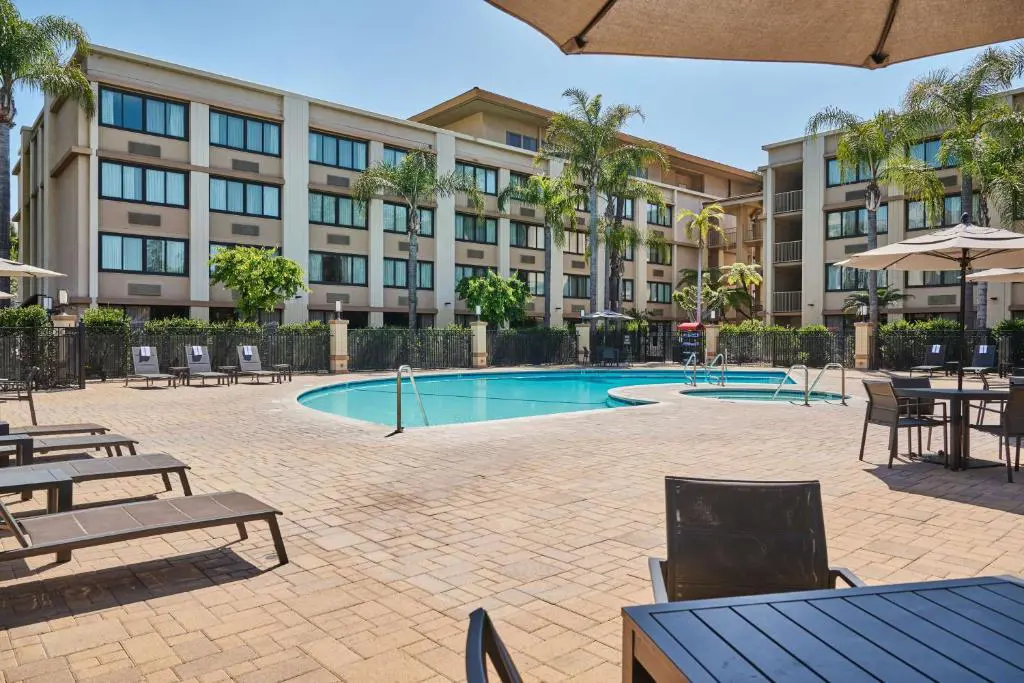 Courtyard view of DoubleTree by Hilton Buena Park featuring an outdoor pool framed by sun loungers and umbrellas, with guest rooms overlooking the pool area