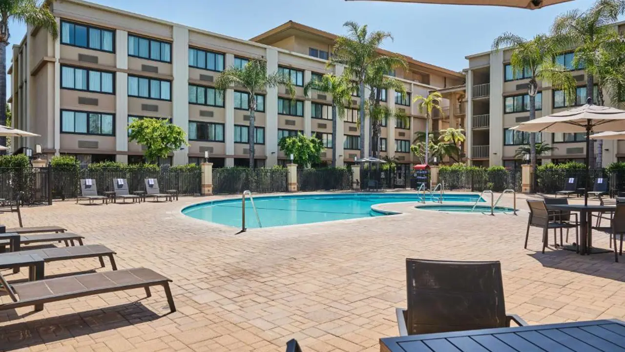 Courtyard view of DoubleTree by Hilton Buena Park featuring an outdoor pool framed by sun loungers and umbrellas, with guest rooms overlooking the pool area