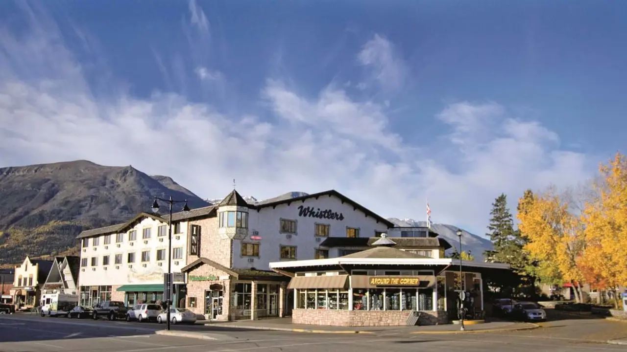 Exterior of Whistler’s Inn in Jasper, Canada, showing a cosy mountain lodge-style building with wooden balconies, surrounded by tall evergreen trees and rugged mountain peaks in the background