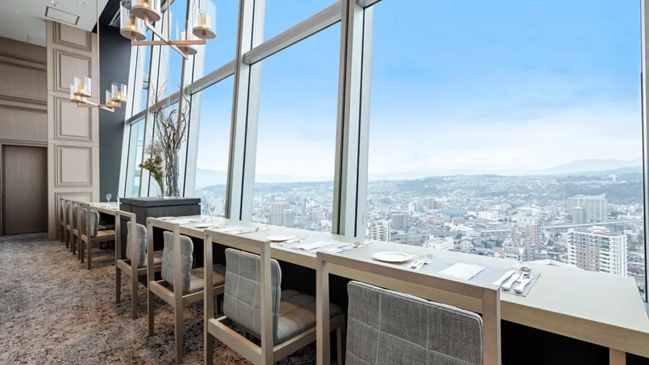 Elegant dining area at Hotel Nikko Ōita Oasis Tower, with floor-to-ceiling windows offering panoramic views over Ōita city, set with modern chairs and white table settings