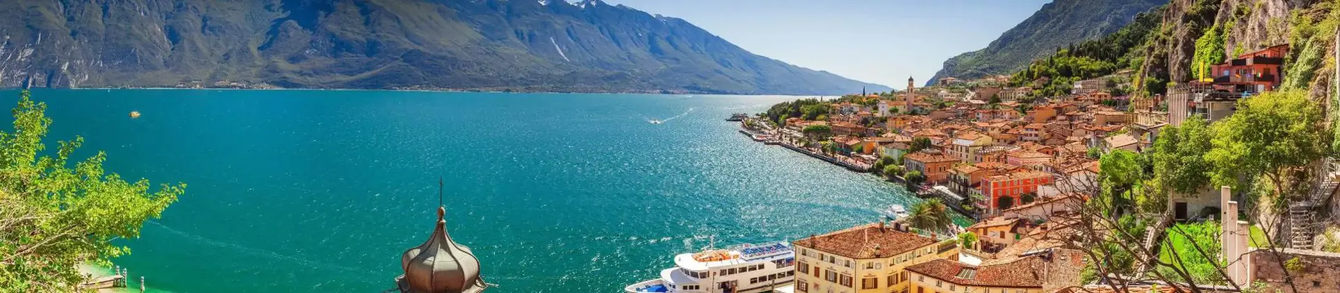 Scenic view of Limone sul Garda, a picturesque lakeside town on Lake Garda, Italy, with colourful buildings nestled against steep mountain cliffs and the calm blue lake in the foreground