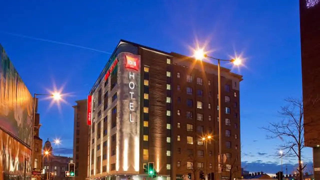 Exterior view of the ibis Belfast City Centre hotel at dusk, with the building lit up and traffic passing by