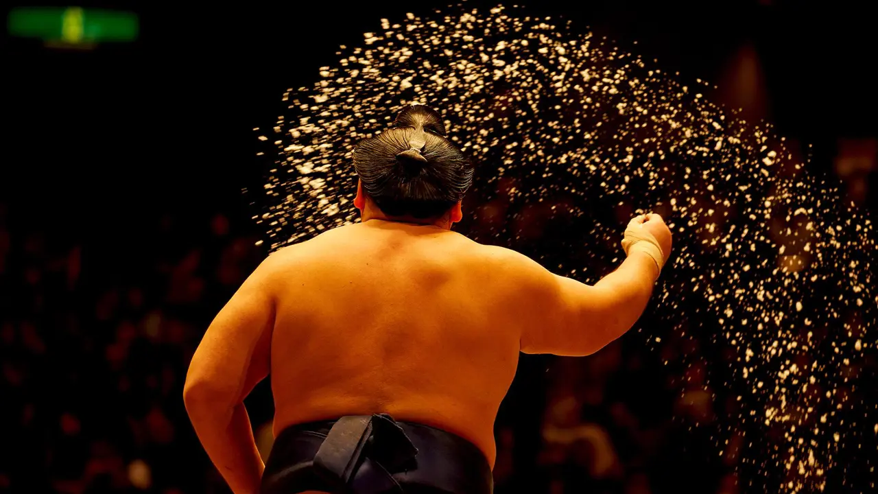 A sumo wrestler viewed from behind, tossing salt into the ring as part of a ritual before a match in Fukuoka, Japan