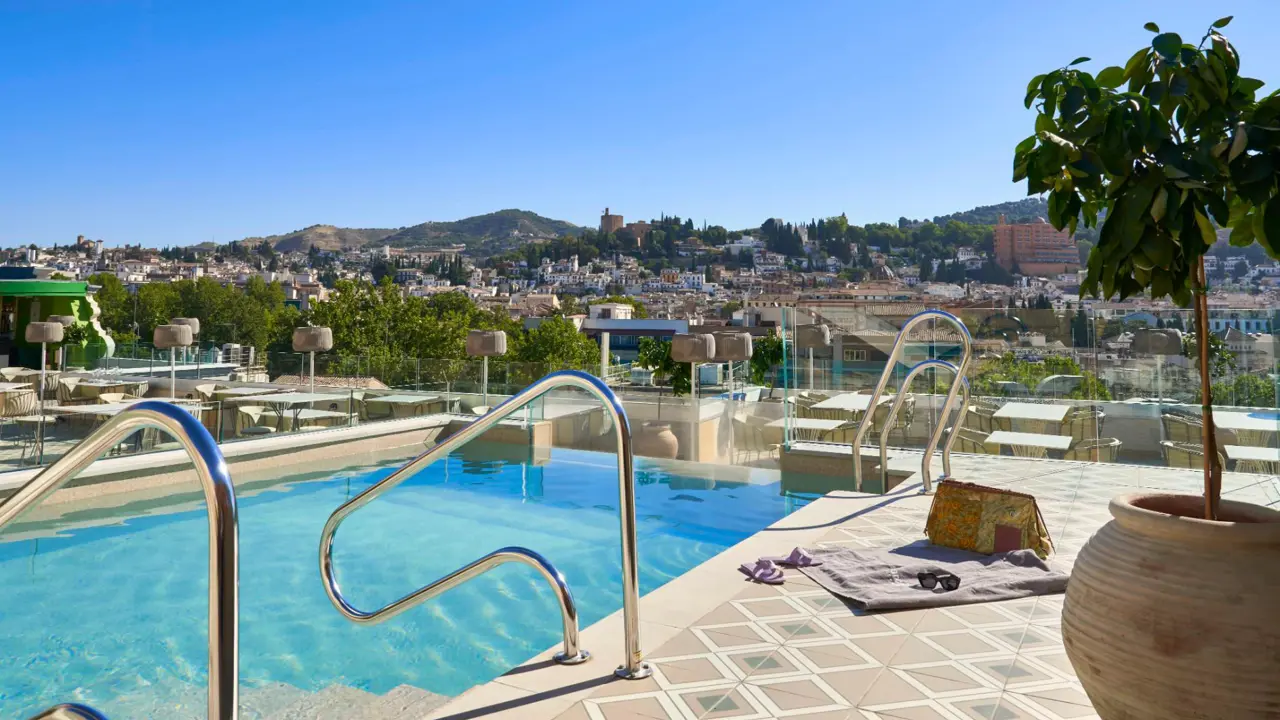The rooftop pool at Barceló Carmen Granada hotel with views of the city and mountains in the distance on a sunny day