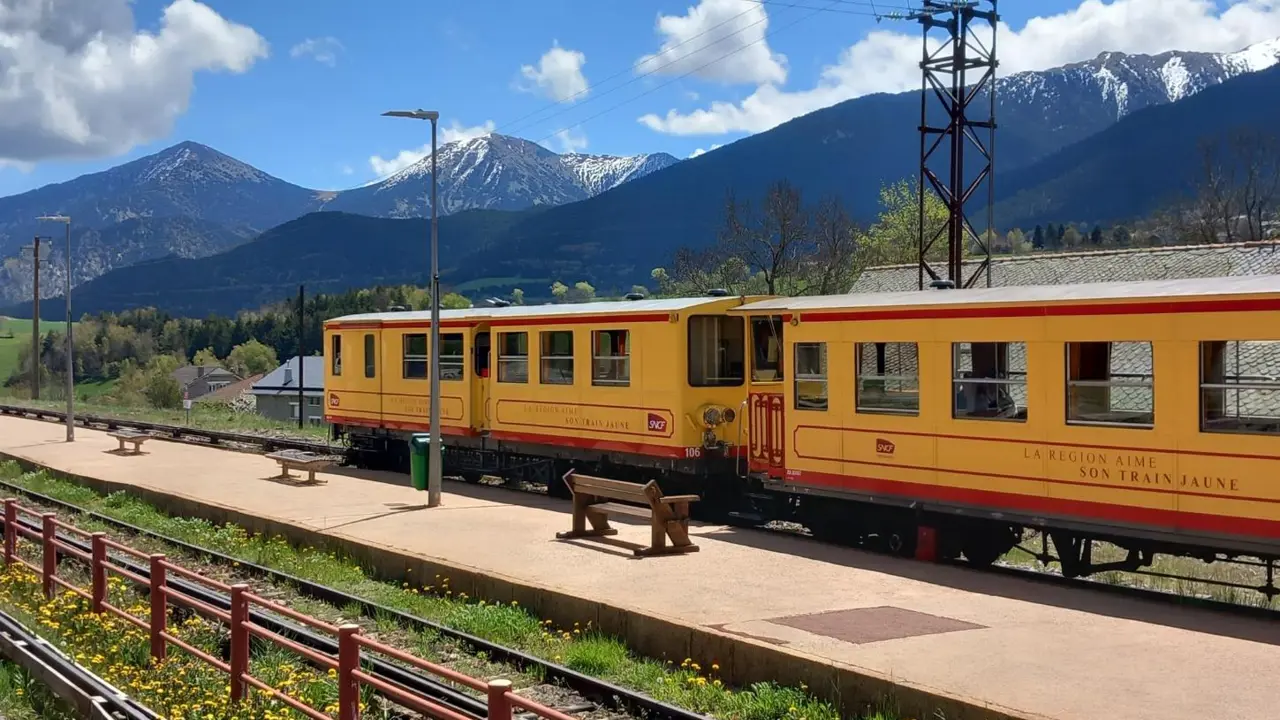 Le Train Jaune at a station with a Pyrenees mountain view