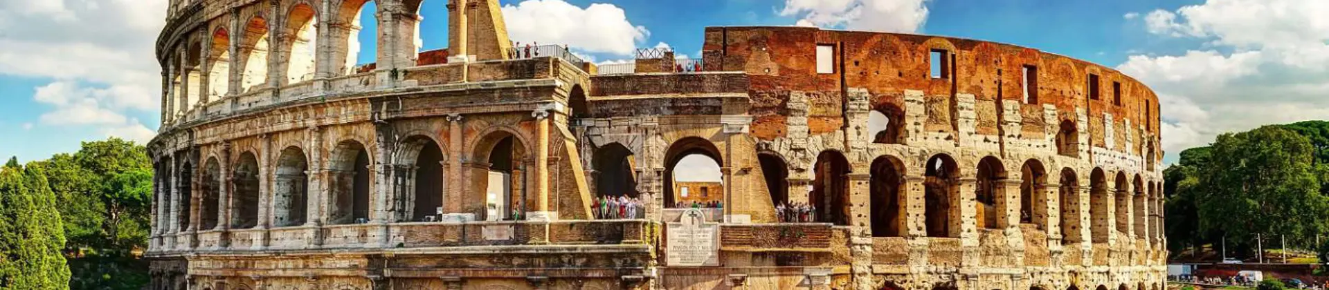 The Colosseum in Rome, a vast ancient Roman amphitheatre with partially preserved stone arches and tiered seating, set against a blue sky with scattered clouds