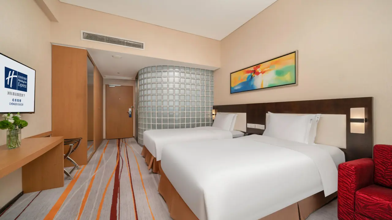 Comfortable twin hotel room with two beds, desk space and a red armchair at the Holiday Inn Express Beijing Gulou Hotel in Beijing, China