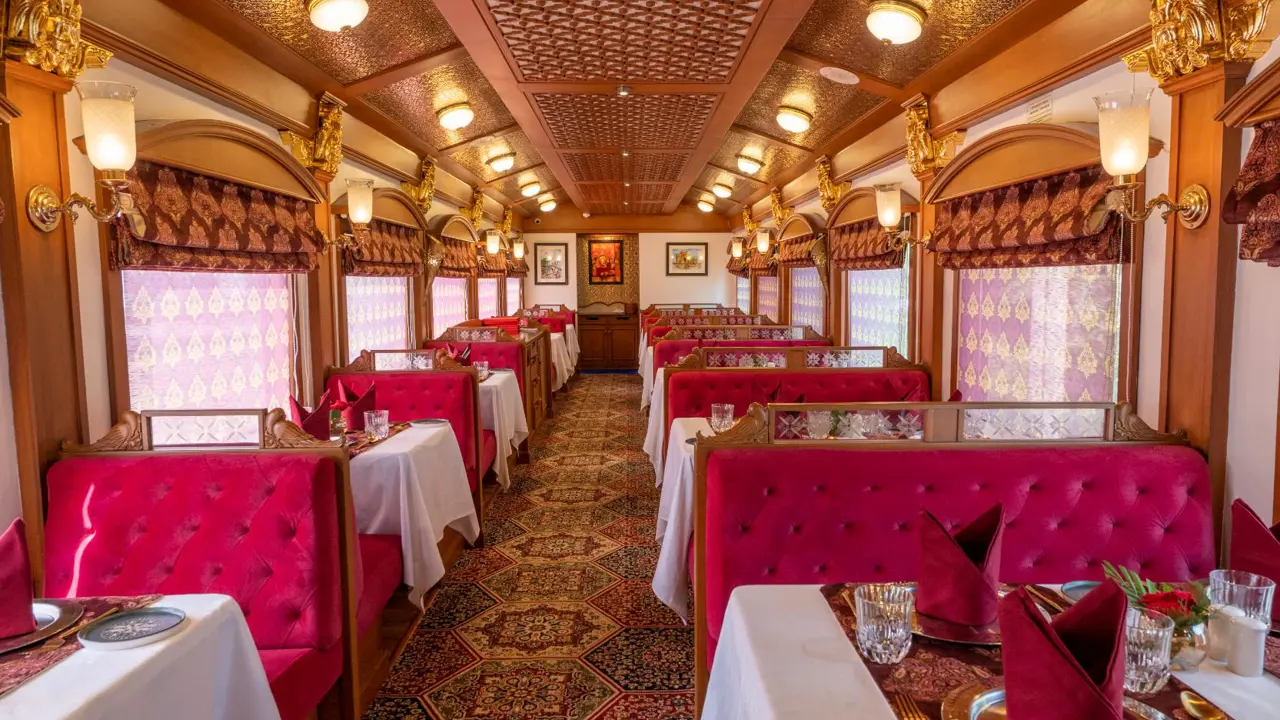 The Deccan Odyssey dining car with red detailing, upholstered seats, patterned curtains, and tables set for meals