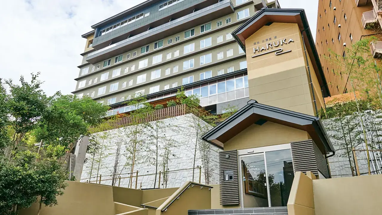 Exterior of the Hotel Kowakuen Haruka in Matsuyama, a multi-storey building nestled on a hillside with landscaped greenery and bamboo in the foreground