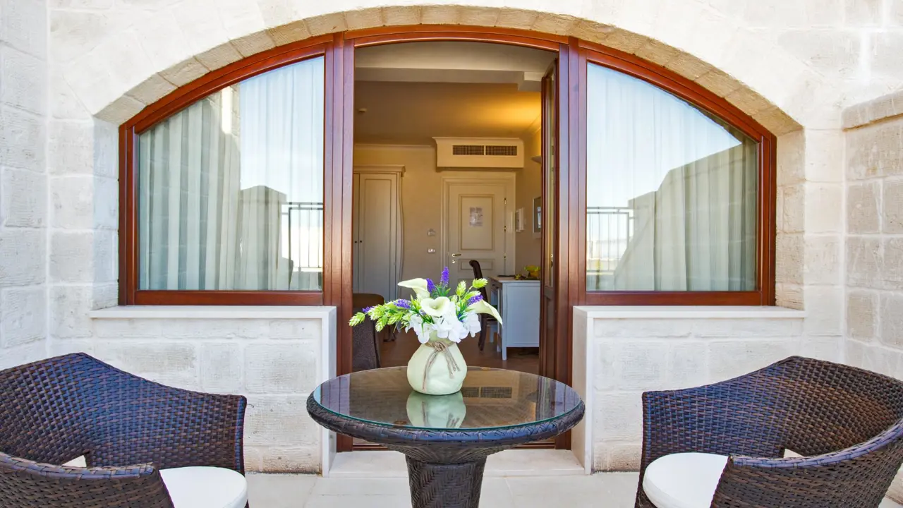 Private terrace at Masseria Caselli Hotel, Italy, with wicker chairs, a glass table, and a vase of fresh flowers