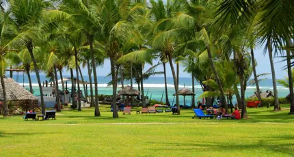 Mombasa Beach, Kenya, featuring an open green space with palm trees and sun loungers, and the clear blue sea beyond