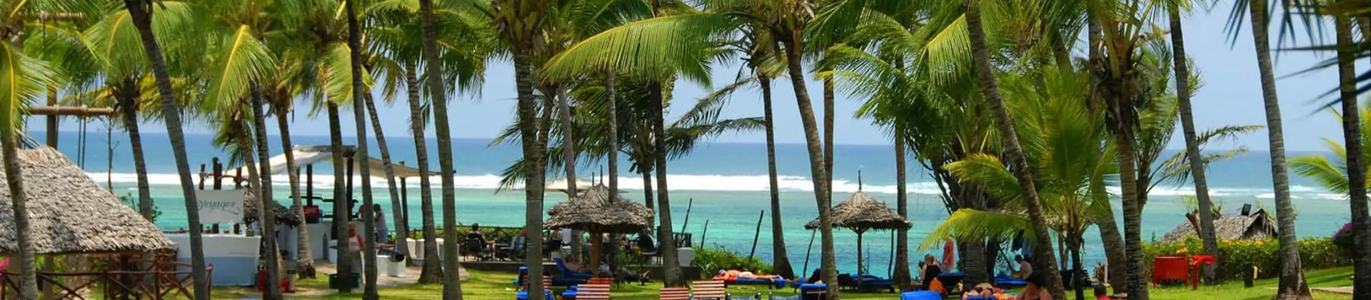 Mombasa Beach, Kenya, featuring an open green space with palm trees and sun loungers, and the clear blue sea beyond