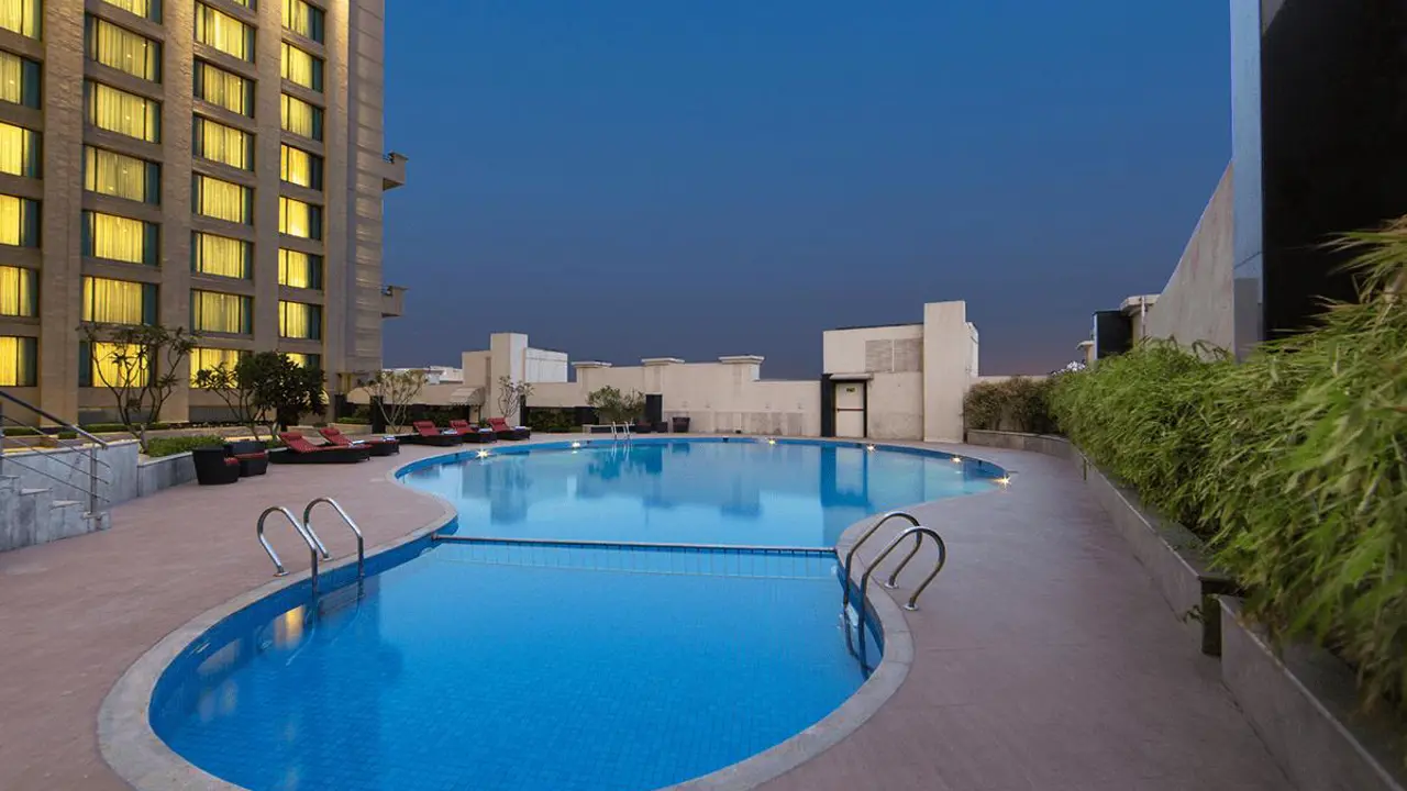 An outdoor swimming pool at WelcomHotel by ITC in Dwarka surrounded by sun loungers and greenery