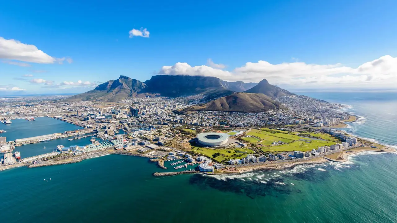 Aerial view of Cape Town, South Africa, showing the city nestled between Table Mountain and the Atlantic Ocean, with the coastline, harbour, and urban landscape clearly visible
